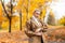 Pretty glamorous young woman with a trendy hairstyle in an elegant coat poses in a white sweater outdoors in a park on a warm