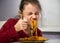Pretty grimacing kid girl eating tasty spaghetti on the dinner on the home kitchen. Closeup