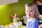 Pretty happy little smiling girl with blond hair in purple shirt standing in kitchen