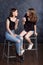 Pretty happy teenage girls with donuts  siting on chairs and having fun. Portrait of joyful smiling girls with donuts on black