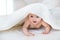 Pretty Infant crawls under a white cover in bed in bedroom