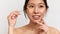Pretty korean lady using cosmetic brush to apply nude eyeshadows, posing over white studio background, closeup