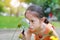 Pretty little Asian child girl with magnifying glass looks at flower in summer park