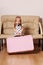 Pretty little blonde girl drags big pink suitcase near sofa