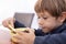 Pretty little boy sitting on chair at table in kitchen and having breakfast closeup. Kid of kindergarten age holding