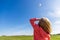 Pretty little girl with blond hair in a field in a pink sweatshirt looks at a colorful kite in a blue sky with soft clouds