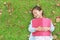 Pretty little girl with book lying on green grass with dried leaves in the summer garden