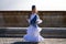A pretty little girl dancing flamenco dressed in a white dress with ruffles and blue fringes in a famous square in seville, spain