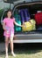 Pretty little girl with pink dress loads suitcases on the car