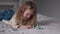 Pretty little girl playing with little christmas trees lying on bed in gray bedroom. new year, childhood, daughter