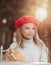 Pretty little girl in a red cap sitting in outdoor cafe with baguette and smiling. French style