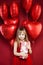 Pretty little girl in red tulle dress with birthday gift and red balloons background. Cute child smiling, birthday party