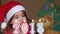 Pretty little girl in a Santa Claus hat blowing out candles. Little girl holding a Christmas teddy bear