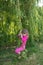 Pretty little girl swinging on weeping saul branches in a garden