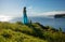 Pretty long haired blonde woman stands in long turquoise dress at the top of a coastal hill. Ireland, natural scene, beautiful lan