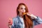 Pretty long redhead ginger girl eating fries chicken in studio pink background