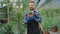 Pretty looking man with a beard gardener in his flower greenhouse very happy taking a plant with a pot from the table