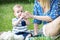 A pretty mather Giving water from a bottle with a pacifier to a baby boy sitting outdoor on grass