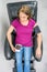Pretty middle-age woman sitting in black leather recliner armchair. Checking blood pressure using portable blood pressure machine.