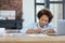 Pretty mixed race teen schoolgirl looking focused, using laptop while making notes during online video lesson at home