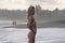 Pretty model in white bikini posing by ocean, standing in half turn to camera,