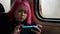 pretty modern little girl with pink hair is riding train and watching cartoons by smartphone