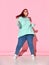 Pretty plump woman with ginger hair in jeans, cosy hoodie and sneakers having much fun jumping on floor, isolated on pink