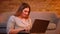 Pretty plus size model sits on floor typing smilingly on laptop being glad with job in cozy home atmosphere.