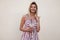 Pretty positive young woman in a trendy summer sundress with a sweet milkshake stands near a vintage wall in the city.