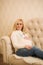 A pretty pregnant blonde in a Christmas sweater sits on sofa