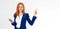 Pretty redhead girl with phone smiling pointing finger right on white background. Young foxy female in business outfit, has amazed