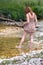 Pretty redhead woman in dress walking on the river barefoot. Young woman walking barefoot, splashing water in mountain river