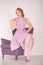 Pretty redheaded pin up woman wearing pink polka dot dress and posing with purple armchair on white background