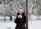 Pretty and rich woman in fur coat is posing near the tree