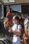 pretty rider with her helmet and vest putting the net on her mare before a competition