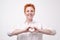 Pretty romantic mature redhead woman making a heart gesture with her fingers in front of her chest showing her love