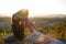 Pretty sad woman in black short summer dress sitting on a rock thinking outdoors at sunset. Fashionable female contemplating in