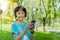 Pretty school girl with smartphone and listens to music with modern headphones wireless in park outdoors