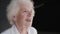 Pretty senior woman speaking at camera with light smile on background