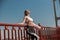 Pretty slim lady with pink mat leans onto railing on modern city footbridge