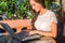 Pretty smiling blogger using laptop computer to write blogs while sitting at outdoor cafe on sunny day.