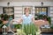 Pretty smiling female in apron standing in front of table with flowers, showing them