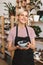 Pretty smiling girl in black apron and striped T-shirt holding handmade plate and bowl in hands happily looking in