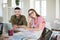 Pretty smiling girl in striped t-shirt and eyeglasses happily closing eyes while working with colleague. Group of cool