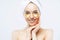 Pretty smiling lady has towel on head touches cheeks, applies golden hydrogel patches, stands shirtless indoor, removes wrinkles,