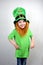 Pretty smiling littel girl in green clothes with decorative red beard in leprechaun\\\'s hat with gold clover leaf.