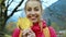 Pretty smiling woman in red jacket standing outdoors, holding a few dry yellow leaves in hands and plays with them