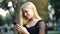 Pretty smiling young blonde in black spring dress is holding a red smartphone in her hands and chatting with friends