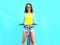 Pretty smiling young woman rides a bicycle over colorful blue