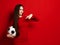 Pretty smug smiling brunette woman in tight red dress holds soccer ball and point her finger at it